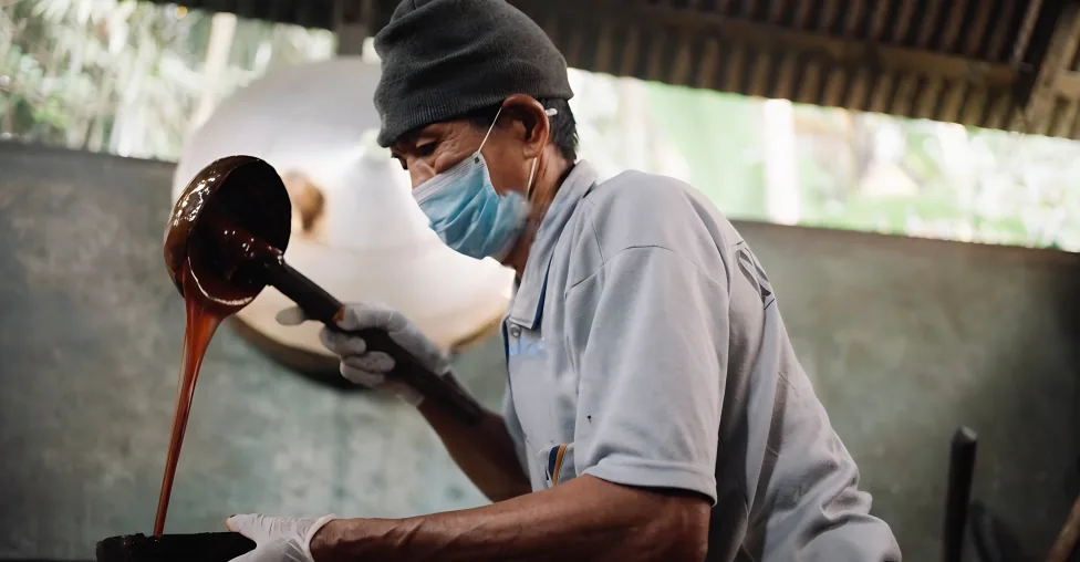A worker pours thick arenga syrup from a ladle