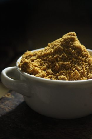 A warm-toned close-up of brown sugar in a ceramic bowl with dramatic lighting.