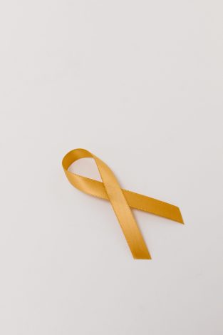 A close-up of a gold awareness ribbon on a white surface symbolizing cancer awareness and support.